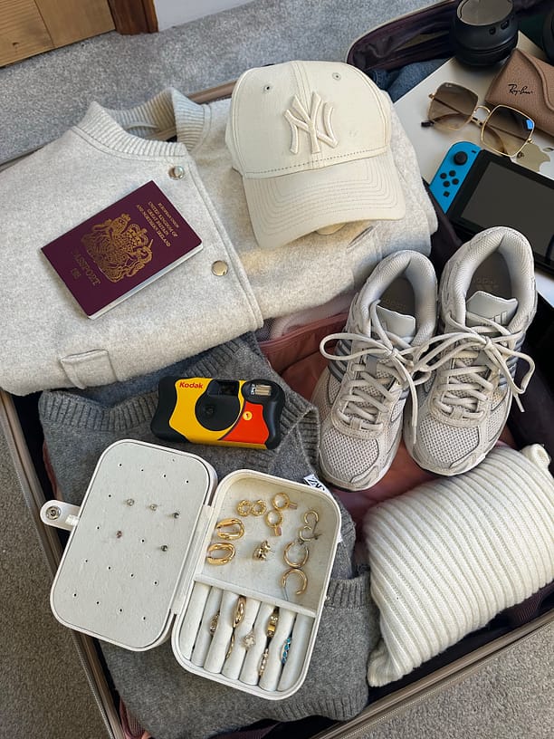 Open suitcase with a jacket, cap, passport, sneakers, camera, jewelry case, and Nintendo Switch